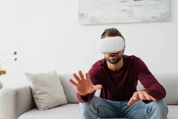 Homme étonné gestuelle alors qu'il était assis sur le canapé dans le casque vr — Photo de stock