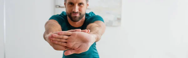 Blurred athletic man looking at camera while stretching at home, banner — Stock Photo