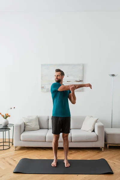 Ganzkörperansicht eines barfüßigen Mannes, der sich zu Hause auf einer Yogamatte dehnt — Stockfoto