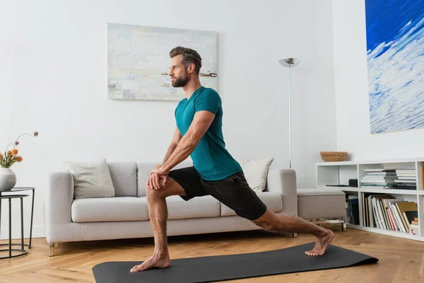 Sportive man practicing crescent lunge pose on yoga mat at home — Stock Photo