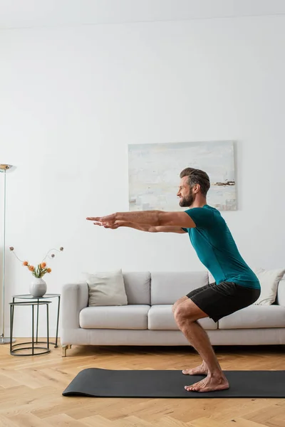 Vista laterale dell'uomo in abbigliamento sportivo praticare posa imbarazzante su tappetino yoga — Foto stock