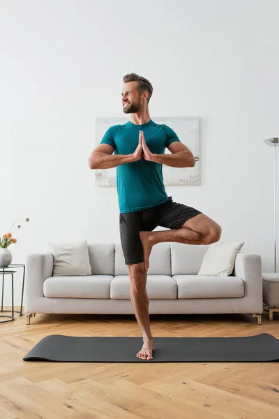 Lächelnder Mann schaut weg, während er in einbeiniger Baumpose steht — Stockfoto