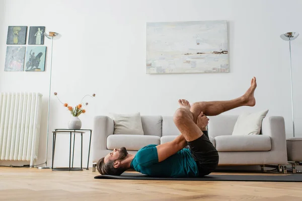 Side view of man practicing pigeon pose on yoga mat at home — Stock Photo