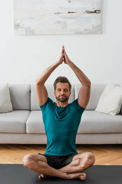 Man with praying hands and closed eyes meditating in lotus pose at home — Stock Photo