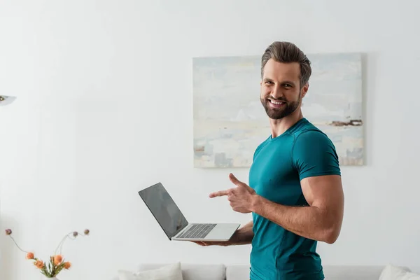 Uomo felice che punta con il dito al computer portatile mentre sorride alla fotocamera — Foto stock