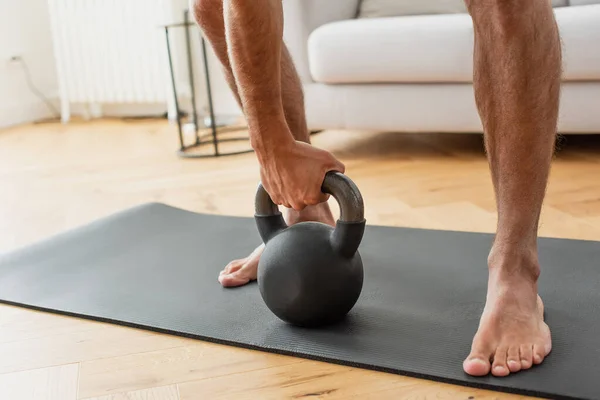 Vue partielle du sportif pieds nus faisant de l'exercice avec kettlebell à la maison — Photo de stock