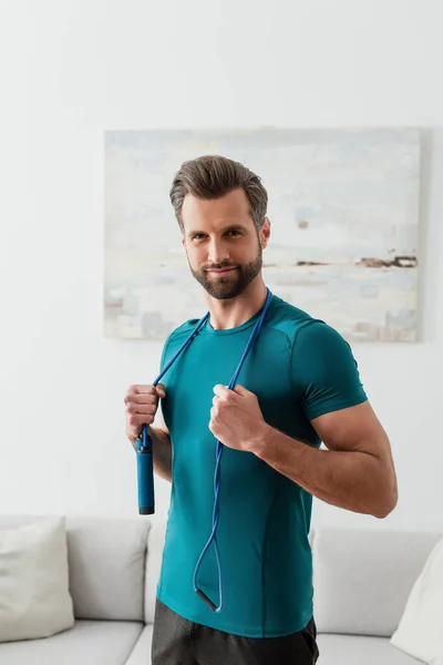 Sportive man with skipping rope smiling at camera at home — Stock Photo
