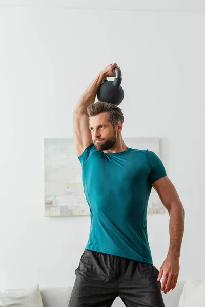 Atlético homem no sportswear trabalhar fora com kettlebells em casa — Fotografia de Stock
