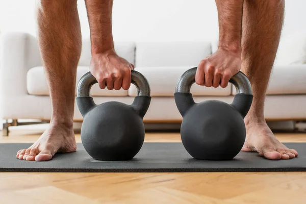 Partial view of barefoot man lifting kettlebells on fitness mat — Stock Photo