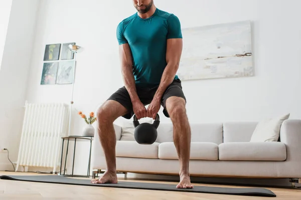 Cropped view of barefoot man lifting kettlebell at home — Stock Photo