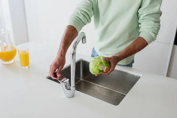 Cropped view of man holding fresh lettuce near sink in kitchen — Stock Photo