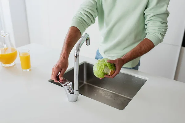 Vista cortada do homem segurando alface fresca perto da pia na cozinha — Fotografia de Stock