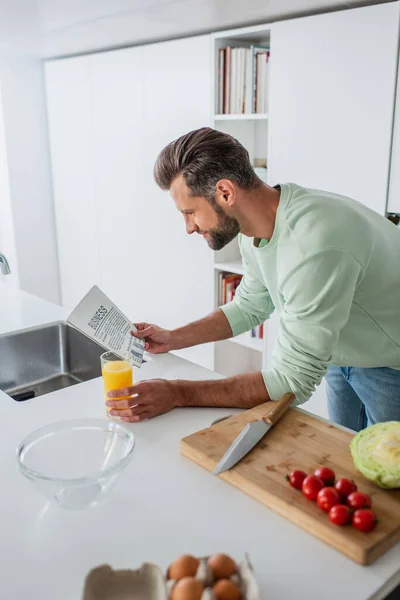 Hombre leyendo noticias de negocios cerca de zumo de naranja y verduras frescas - foto de stock