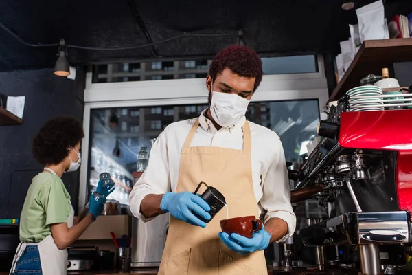 Африканская американская бариста в медицинской маске готовит кофе в кафе — стоковое фото