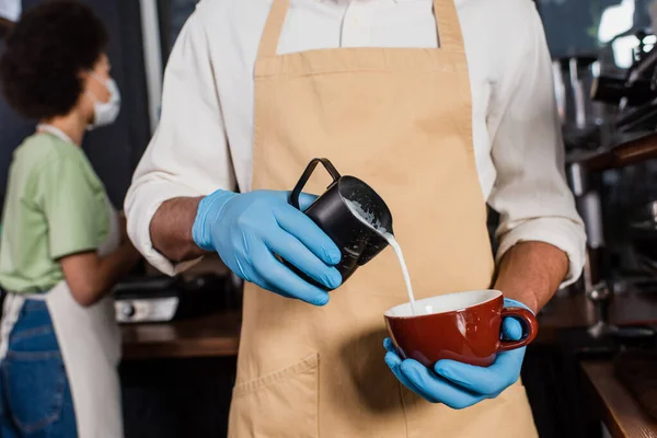 Barista afro-américaine en gants de latex faisant du café avec du lait dans le café — Photo de stock
