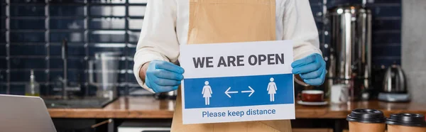 Cropped view of african american barista in latex gloves holding signboard with we are open lettering in cafe, banner — Stock Photo