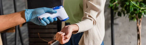 Ausgeschnittene Ansicht eines afrikanisch-amerikanischen Kellners in Latex-Handschuh mit Infrarot-Thermometer in der Nähe des Kunden im Café, Banner — Stockfoto