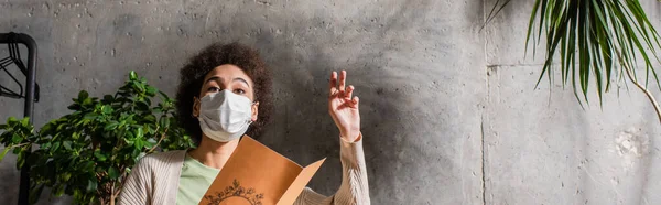 Cliente afro-americano em máscara médica segurando menu no café, banner — Fotografia de Stock