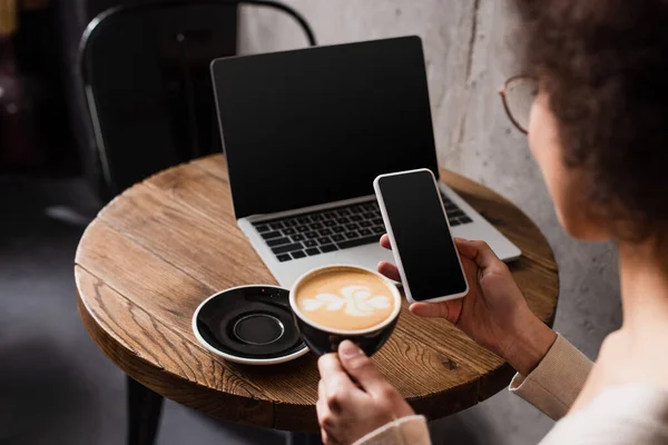 Smartphone y café en manos del borroso afroamericano freelancer en la cafetería - foto de stock