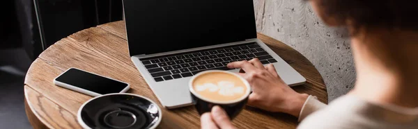 Vista cortada da mulher americana africana borrada com café usando laptop no café, banner — Fotografia de Stock