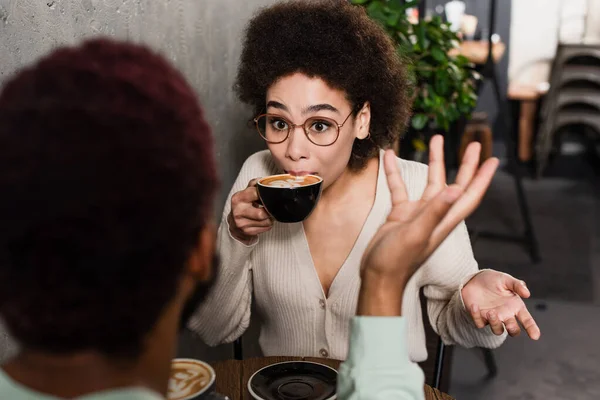 Mujer afroamericana bebiendo café cerca de novio borroso en la cafetería - foto de stock