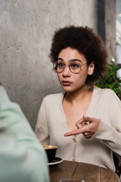 African american woman pointing at coffee near blurred boyfriend in cafe — Stock Photo