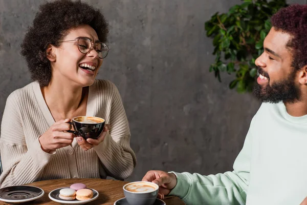 Весела афроамериканська пара з кавою, що розмовляє біля макаронів у кафе. — стокове фото