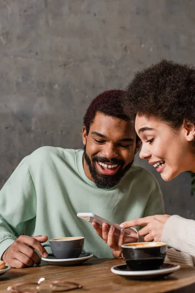 Positivo casal afro-americano usando smartphone perto de xícaras de café no café — Fotografia de Stock