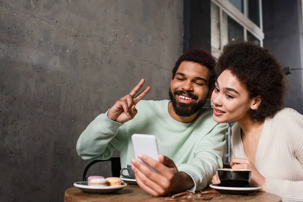 Улыбающаяся африканская американская пара делает селфи на смартфоне в кафе — стоковое фото