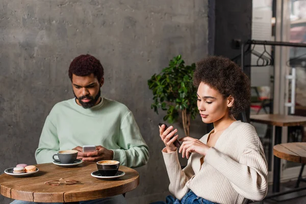 African american woman using smartphone near boyfriend and coffee in cafe — Stock Photo