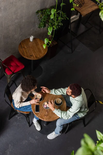 Overhead view of african american man pointing at girlfriend with coffee in cafe — Stock Photo