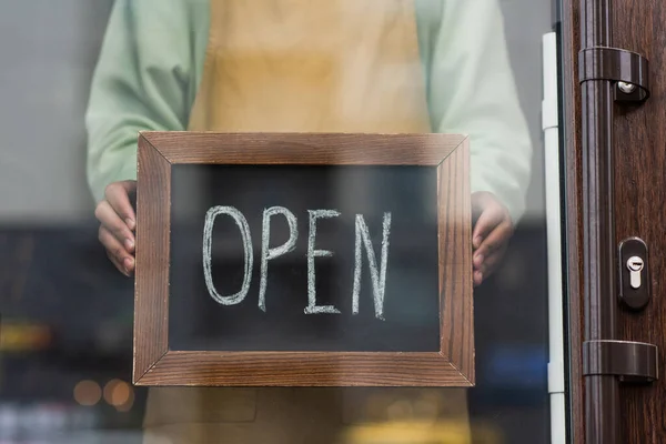 Cropped view of african american barista holding chalkboard with open lettering in cafe — Stock Photo