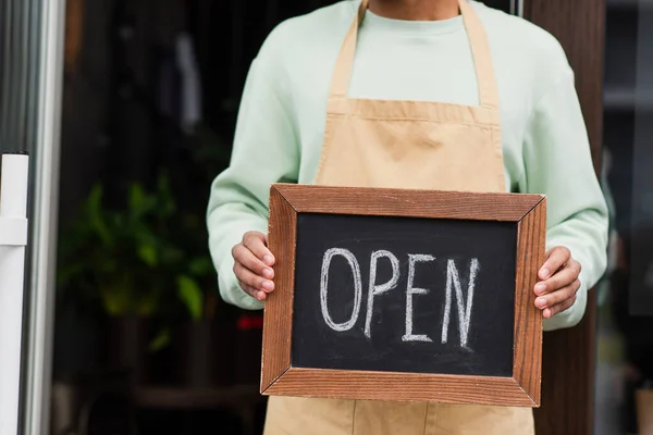 Cropped view of african american barista holding chalkboard with open lettering near cafe — Stock Photo