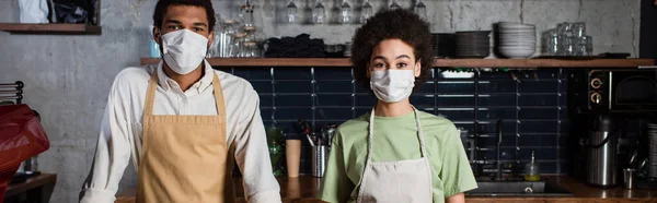 African american baristas in medical masks looking at camera in cafe, banner — Stock Photo