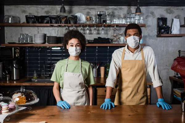 Baristas afro-americanos em luvas de látex e máscaras médicas em pé no café — Fotografia de Stock