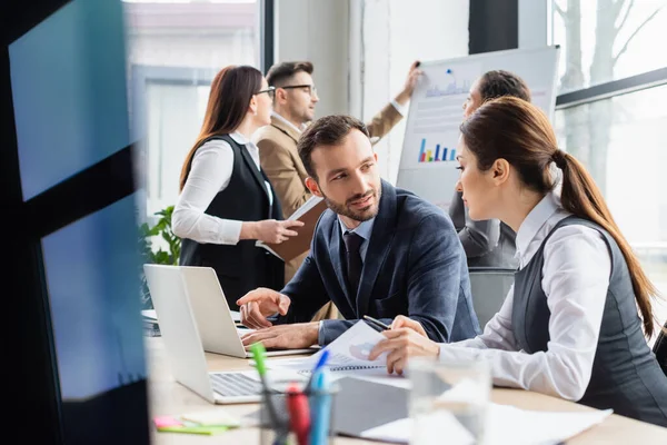 Empresario hablando con colega cerca de papeles y portátiles - foto de stock