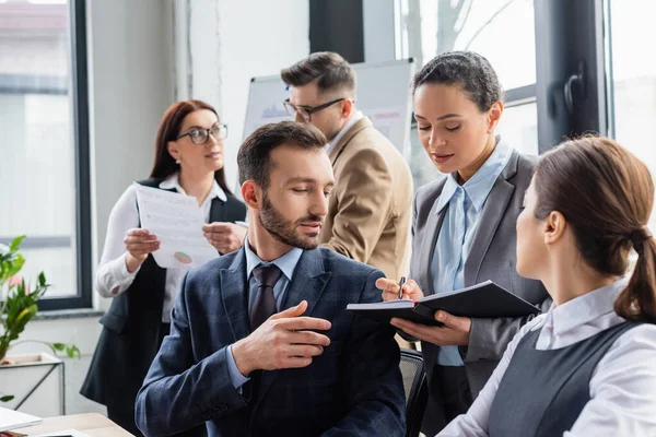 African american businesswoman holding notebook near colleagues in office — Stock Photo