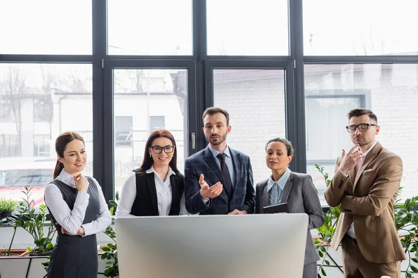 Geschäftsmann zeigt auf Computer neben fröhlichen multiethnischen Kollegen im Büro — Stockfoto