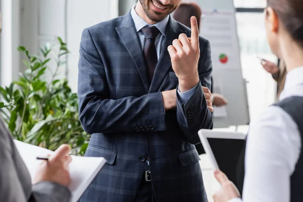 Smiling businessman pointing with finger near blurred colleagues with digital tablet and notebook — Stock Photo