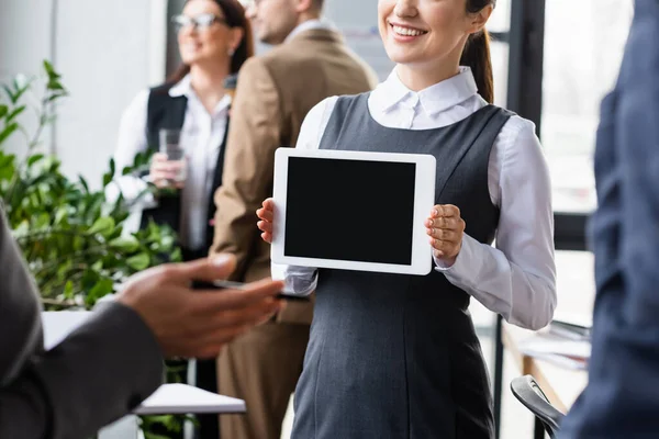 Mujer de negocios sonriente sosteniendo tableta digital cerca de colegas borrosos en la oficina — Stock Photo