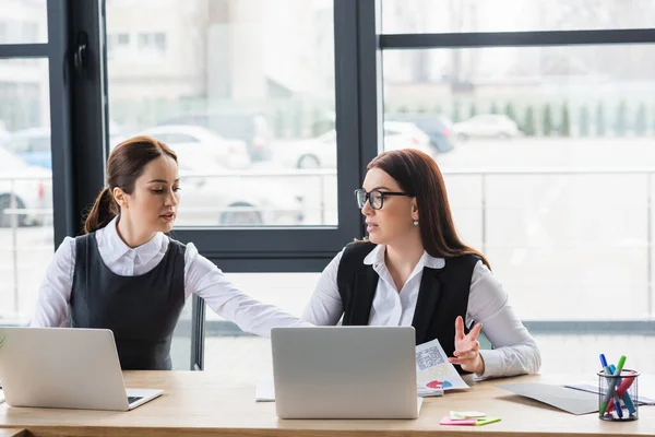 Femmes d'affaires travaillant avec des papiers près des ordinateurs portables sur la table — Photo de stock