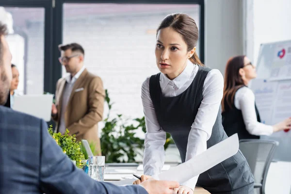 Imprenditrice che guarda un collega sfocato con un documento mentre lavora in ufficio — Foto stock