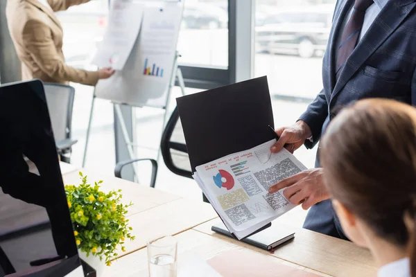Businessman pointing at paper with charts near blurred colleague in office — Stock Photo