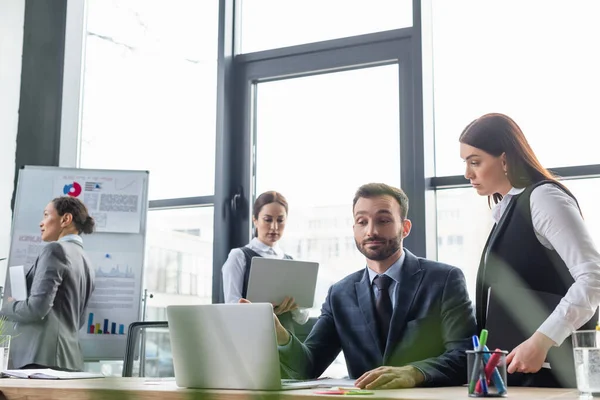 Businesswoman with paper folder looking at colleague near laptop in office — Stock Photo