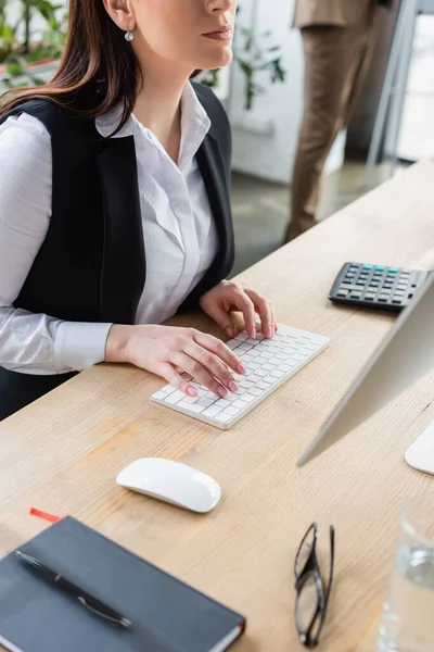 Cropped view of businesswoman using computer near notebook and eyeglasses in office — Stock Photo