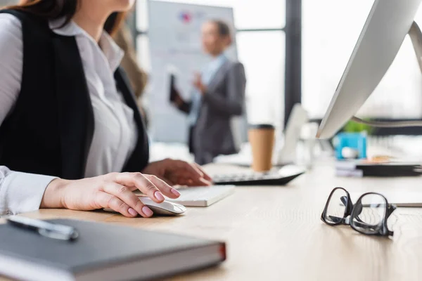 Vista recortada de la mujer de negocios utilizando la computadora cerca de las gafas y el cuaderno borroso - foto de stock