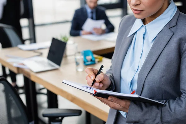 Ausgeschnittene Ansicht einer afrikanisch-amerikanischen Geschäftsfrau, die auf ein Notizbuch schreibt — Stockfoto