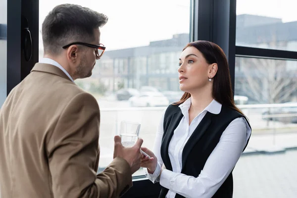 Businesswoman with smartphone talking to colleague with glass of water — Stock Photo