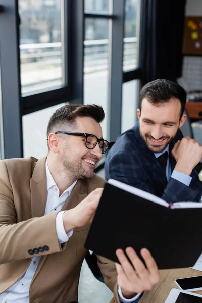 Smiling businessman holding blurred notebook near colleague — Stock Photo