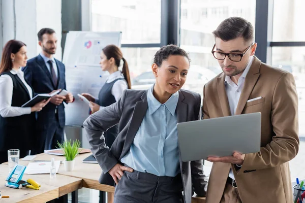 Donna d'affari afroamericana in cerca di laptop vicino al collega in carica — Stock Photo